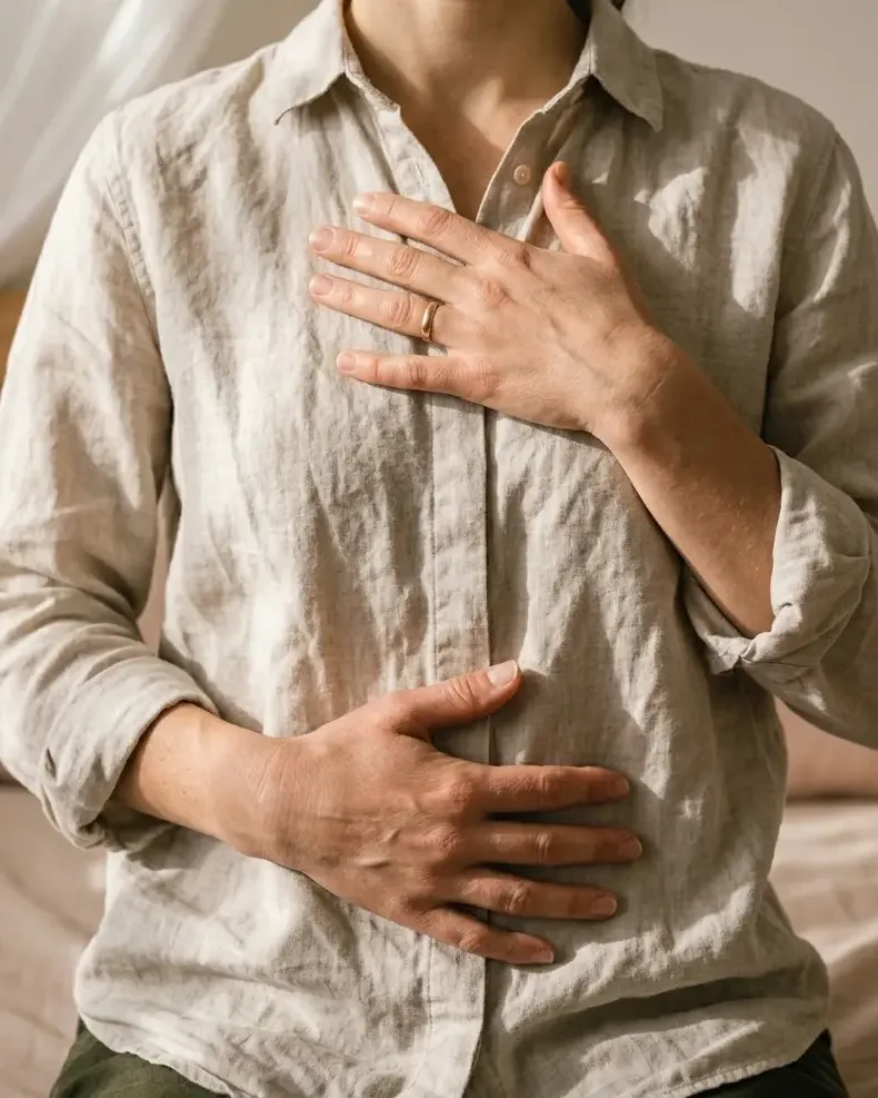 Des mains posées sur la poitrine et le ventre, dans une lumière douce, pour une respiration profonde.