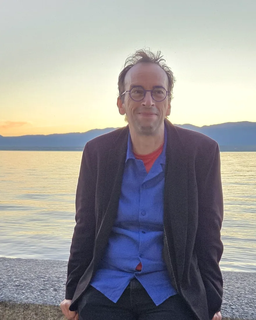 Vincent Vocat, souriant, adossé à un muret au bord du Léman au coucher du soleil.
